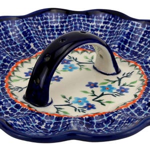 May include: A blue and white ceramic serving dish with a scalloped edge and a handle. The dish features a blue and white checkered pattern on the outer rim and a floral design in the center. The handle is dark blue.