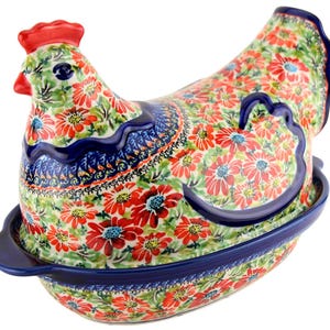 May include: A ceramic hen-shaped serving dish with a lid, featuring a vibrant floral pattern in red, green, and blue. The dish has a dark blue rim and handle, and a red comb. This decorative piece is ideal for kitchen decor.