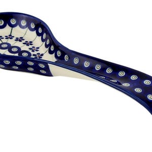 May include: A ceramic spoon rest with a curved handle. The spoon rest is primarily dark blue with a white interior and floral patterns. The handle and rim feature a repeating pattern of white and green circles.