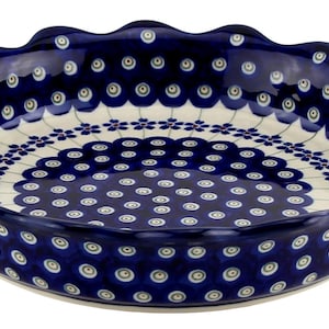 May include: A round, ceramic pie dish with a scalloped edge. The dish features a dark blue background with a white and blue floral pattern. The interior has a white base with a blue floral design. A decorative kitchenware item.