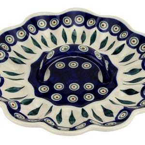 May include: A white ceramic serving dish with a scalloped edge and a handle. The dish features a blue and white floral pattern with green accents. The handle is a solid blue color with a matching pattern. This decorative dish is ideal for serving snacks or appetizers.