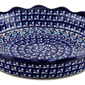 May include: A round, ceramic pie dish with a scalloped edge. The dish features a dark blue base with a detailed pattern of white, light blue, and dark blue floral and geometric designs. The dish is designed for baking.