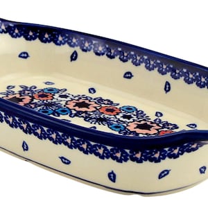 May include: Cream-colored ceramic baking dish with a blue floral design and a dark blue rim. The dish has a rectangular shape with curved edges and handles. The floral pattern includes pink and blue flowers.