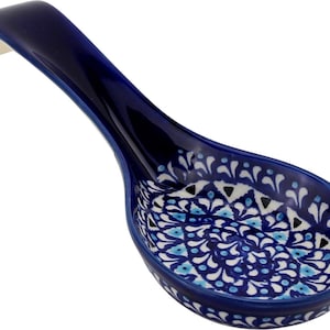 May include: A ceramic spoon rest featuring a deep blue exterior and a handle. The interior bowl displays a detailed, symmetrical pattern in shades of blue, white, and black, characterized by intricate floral and geometric motifs across the surface.