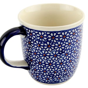 May include: A ceramic mug with a blue floral pattern. The mug has a white interior and a dark blue handle. The floral design features white flowers with orange centers on a blue background. The mug is designed for hot beverages.