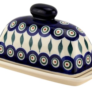 May include: A ceramic butter dish with a domed lid and a rectangular base. The lid is navy blue with a repeating pattern of white, green, and red circles. The base is off-white with a navy blue trim. The lid has a navy blue knob.