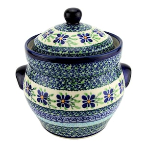 May include: A ceramic jar with a lid, featuring a cream-colored base decorated with blue flowers, green leaves, and intricate blue and green speckled patterns. The jar has two dark blue side handles and a matching dark blue knob on the lid.