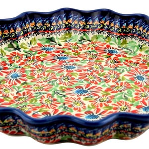 May include: A ceramic pie dish with a scalloped edge. The dish features a floral pattern of red, blue, and green flowers on a white background. The rim is a deep blue with a decorative border. This dish is perfect for baking and serving pies.