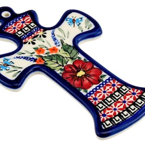 May include: A ceramic cross wall hanging featuring a cream-colored base with a hand-painted design of a large red flower, green leaves, and two small blue butterflies. The edges are outlined in dark blue, with red and white geometric patterns.