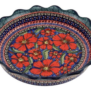 May include: A round ceramic pie dish with a scalloped edge. The dish features a vibrant floral design with red flowers and green leaves on a blue background. The rim has a decorative pattern in blue and red.