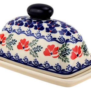 May include: A ceramic butter dish with a domed lid and a rectangular base. The dish is decorated with a floral pattern featuring red flowers, blue accents, and green leaves. The lid has a dark blue knob.