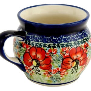 May include: A ceramic mug with a rounded shape and a dark blue handle. The mug features a floral pattern with red poppies, green leaves, and blue accents. The rim and handle are dark blue.