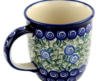 May include: A ceramic mug with a blue handle and rim, featuring a floral pattern in blue and green. The mug has a cream-colored interior and is designed for hot beverages.