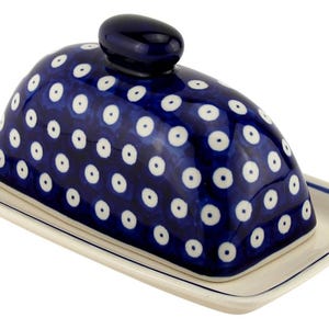 May include: A ceramic butter dish with a navy blue lid adorned with white polka dots. The lid has a small, rounded handle. The base is rectangular and off-white with a blue trim. This dish is designed for serving butter.