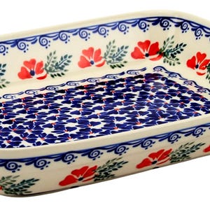 May include: Rectangular ceramic baking dish with a cream-colored base. The dish features a blue and white floral pattern on the interior and exterior, with red poppy accents. The rim is decorated with a blue scroll design.