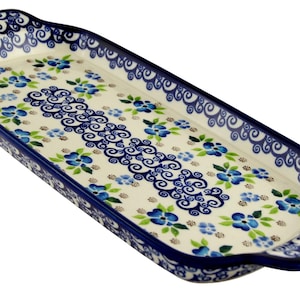 May include: Rectangular ceramic serving tray with a blue floral pattern. The tray has a cream-colored base with blue flowers and green leaves. The edges and handles are dark blue with a decorative scroll design.