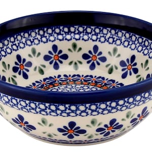 May include: A ceramic bowl with a dark blue rim and a white interior decorated with blue and orange floral patterns. The bowl's design includes a band of blue geometric shapes and green leaf accents.