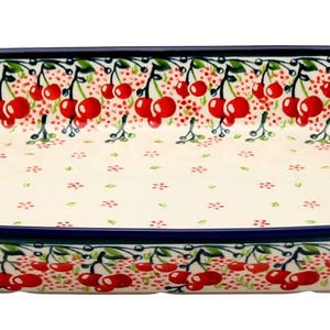 May include: Rectangular ceramic serving dish with a cherry pattern. The dish has a cream-colored interior with a repeating pattern of red cherries and green leaves. The rim is dark blue, and the overall design is a classic, decorative style.