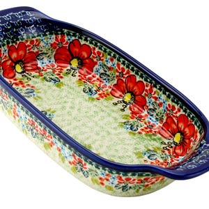 May include: An oblong ceramic baking dish with a floral design. The dish features a light green interior with red flowers and blue and red accents. The rim and handles are dark blue.