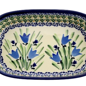 May include: Oval ceramic serving dish with a blue floral design. The dish features a cream-colored interior with blue bellflower illustrations and green leaves. The rim is decorated with blue and green patterns.