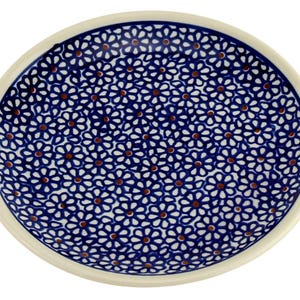 May include: A round ceramic plate with a white rim and a blue floral pattern. The pattern consists of small white flowers with brown centers, densely packed across the plate's surface. The plate is suitable for serving food.