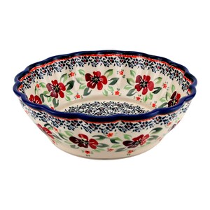 May include: A round ceramic bowl with a scalloped rim, featuring a cream-colored base decorated with red flowers, green leaves, and small blue speckled patterns. The rim is painted with a solid dark blue band, and the interior is patterned.