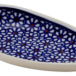 May include: A teardrop-shaped ceramic dish featuring a deep blue interior decorated with a repeating pattern of white daisy-like flowers with small brown centers. The exterior rim and base of the dish are a solid, neutral off-white ceramic color.