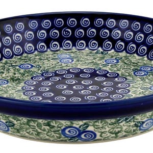 May include: A round ceramic serving bowl with a dark blue rim and a decorative floral pattern. The bowl features a repeating swirl design around the rim and a central floral motif in shades of blue and green.