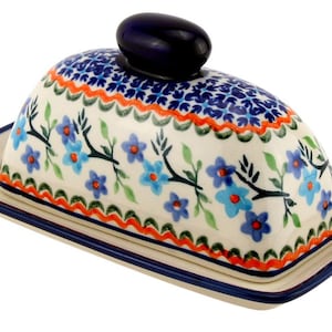 May include: A ceramic butter dish with a lid, featuring a floral design in blue, orange, and green on a white background. The lid has a dark blue knob. The base and lid are rectangular with a dark blue trim.