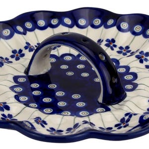 May include: A ceramic serving dish with a scalloped edge and a handle. The dish is white with a blue floral pattern and a dark blue rim. The handle is dark blue with holes. A decorative piece for serving food.