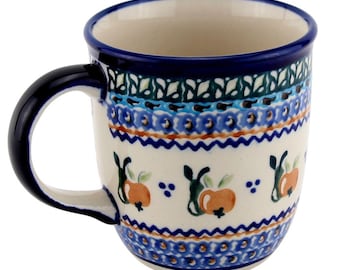 May include: A ceramic mug with a dark blue handle and rim, featuring a cream-colored body. The mug is adorned with a repeating pattern of orange fruit and blue floral designs, with bands of blue and green decorative elements.