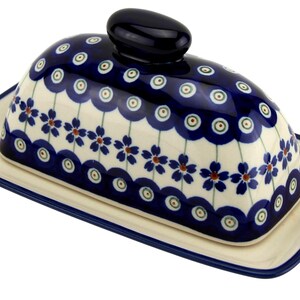 May include: A ceramic butter dish with a navy blue lid and base, adorned with a floral pattern in blue, white, and red. The lid features a rounded handle. The dish is rectangular with a navy blue trim.