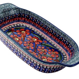 May include: A blue ceramic baking dish with a floral design. The dish features a rectangular shape with handles and is decorated with red flowers and green leaves on a blue background. The rim has a patterned border.