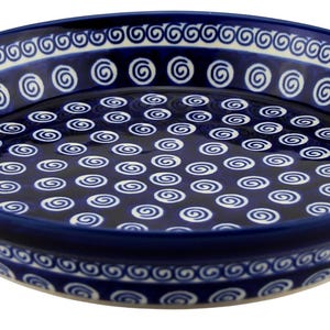 May include: A round, ceramic serving dish with a deep blue glaze. The dish features a repeating white spiral pattern across the interior and along the rim. The rim also has a decorative white scroll design. A classic piece for serving.
