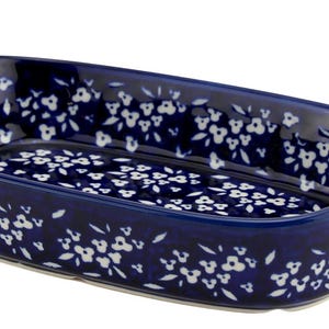 May include: A navy blue ceramic baking dish with a floral pattern. The rectangular dish has curved sides and handles on each end. White floral designs are scattered across the surface.
