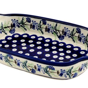 May include: An oval ceramic baking dish with a white base, adorned with blue floral patterns and a scalloped rim. The interior features a dark blue dotted design. The dish has handles on each end and is approximately 10 inches long.