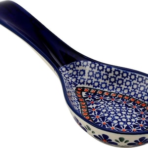 May include: A ceramic spoon rest with a deep blue handle and a bowl featuring a white, blue, and orange floral pattern. The interior of the bowl displays a repeating geometric star design surrounding a central teardrop shape filled with small flowers.