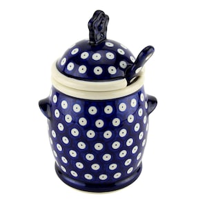 May include: A blue ceramic sugar bowl with a lid and spoon. The bowl is decorated with white polka dots and has two small handles. The lid has a decorative handle. The spoon rests on the rim of the bowl. The sugar bowl is a kitchenware item.
