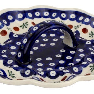 May include: Ceramic serving dish with a handle, featuring a scalloped edge and a vibrant blue and white floral pattern. The dish has a dark blue handle and is decorated with red and green accents.