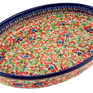 May include: Oval ceramic serving dish with a floral pattern. The dish features a vibrant design of red flowers with blue centers and green leaves on a cream background. The rim is a deep blue with a decorative border.