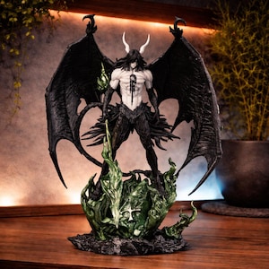 Puede incluir: Figura detallada de un personaje con grandes alas negras, cuernos blancos y un físico musculoso. La figura se alza sobre una base verde en forma de llama. El personaje tiene pelo largo y negro y sostiene un objeto verde.
