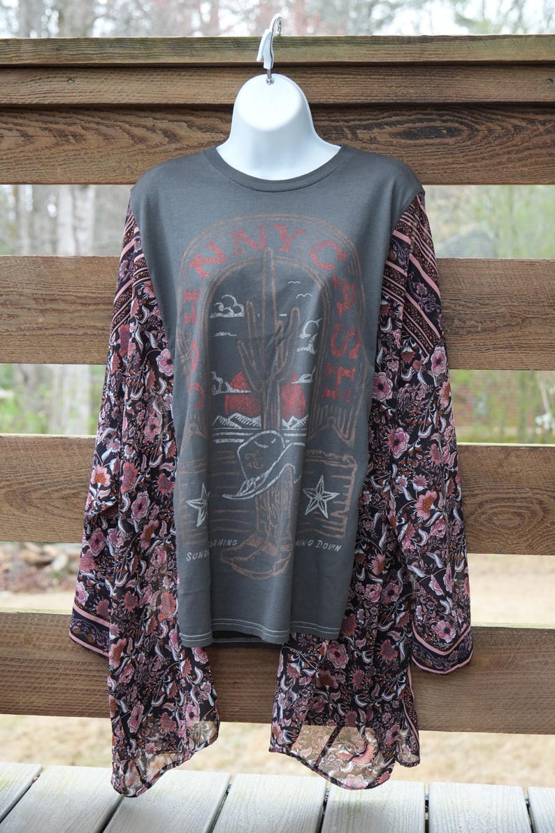 May include: Gray long-sleeve shirt with a graphic of a cactus, cowboy hat, and stars. The sleeves are patterned with a floral design in shades of pink, black, and white. The shirt has the text "SAVOY" and "SUN GOING DOWN".