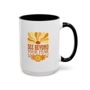 Puede incluir: Taza de cerámica blanca con interior y asa negros. La taza presenta un diseño retro con un gráfico de sol en tonos naranja y amarillo, y el texto "SEE BEYOND YOUR FEAR". Un borde floral en naranja y amarillo completa el diseño.