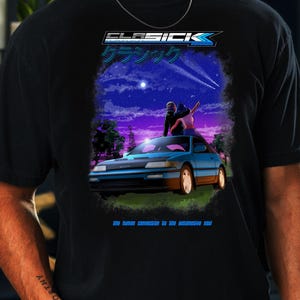 May include: Black t-shirt with a graphic of a blue car and a couple under a starry night sky. The shirt features the text "ELASICK" and Japanese characters. The phrase "the human connection to the automotive soul" is also present.
