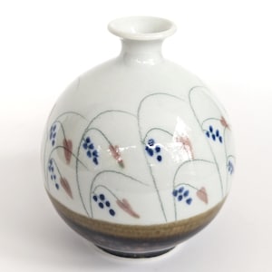 May include: A small, round, white ceramic vase with a brown and black glaze at the base. The vase is decorated with a floral pattern of blue and pink flowers and thin, white lines.