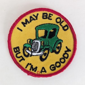 May include: Circular embroidered patch with a yellow background and a red border. It features a green vintage car illustration. Black text arcs around the car, reading "I MAY BE OLD BUT I'M A GOODY."