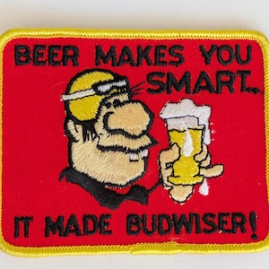 May include: A rectangular embroidered patch with a red background and yellow border. It features a cartoon character holding a glass of beer with white foam. The text reads: BEER MAKES YOU SMART... IT MADE BUDWISER! The design uses black, yellow, and white thread.