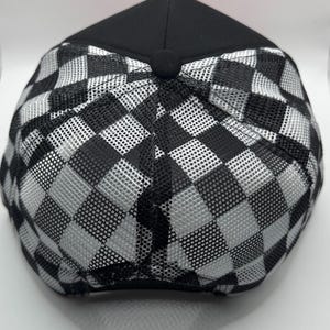 May include: Black and white checkered baseball cap. The cap features a black crown and a mesh back with a checkerboard pattern. The cap is viewed from the top, showcasing the design and construction.