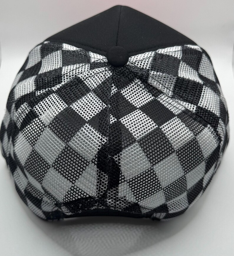 May include: Black and white checkered baseball cap. The cap features a black crown and a mesh back with a checkerboard pattern. The cap is viewed from the top, showcasing the design and construction.