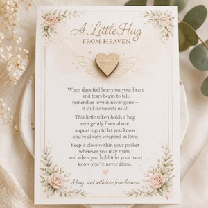 May include: A card featuring the text "A Little Hug From Heaven" and a wooden heart with wings. The card is decorated with floral elements and a poem about love and remembrance. The color palette is soft and pastel.